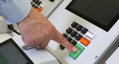 Foto de uma mão masculina apertando o botão verde de ''confirma'' na urna eletrônica com o dedo ...