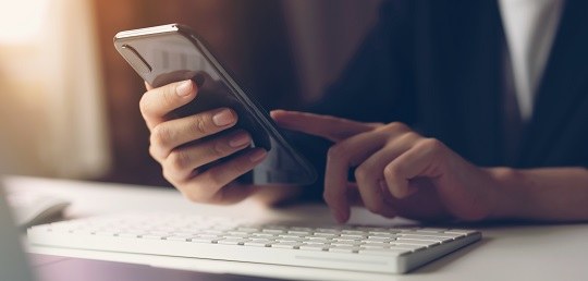 Fotografia de uma pessoa manipulando um telefone celular em cima de um teclado