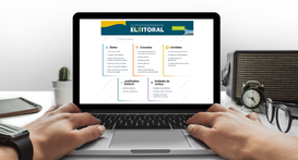 A imagem mostra um computador portátil sobre uma mesa com duas mãos posicionadas sobre o teclado...